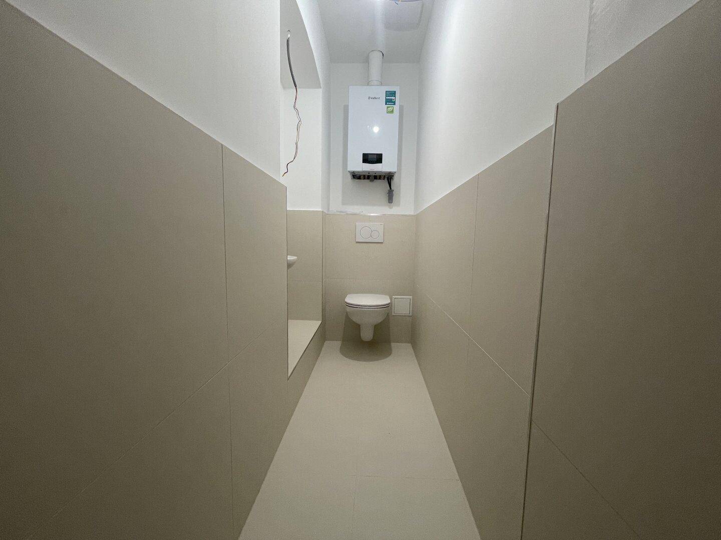 Schmaler Toilettenraum mit Wand-WC und Gastherme, funktional und platzsparend gestaltet.