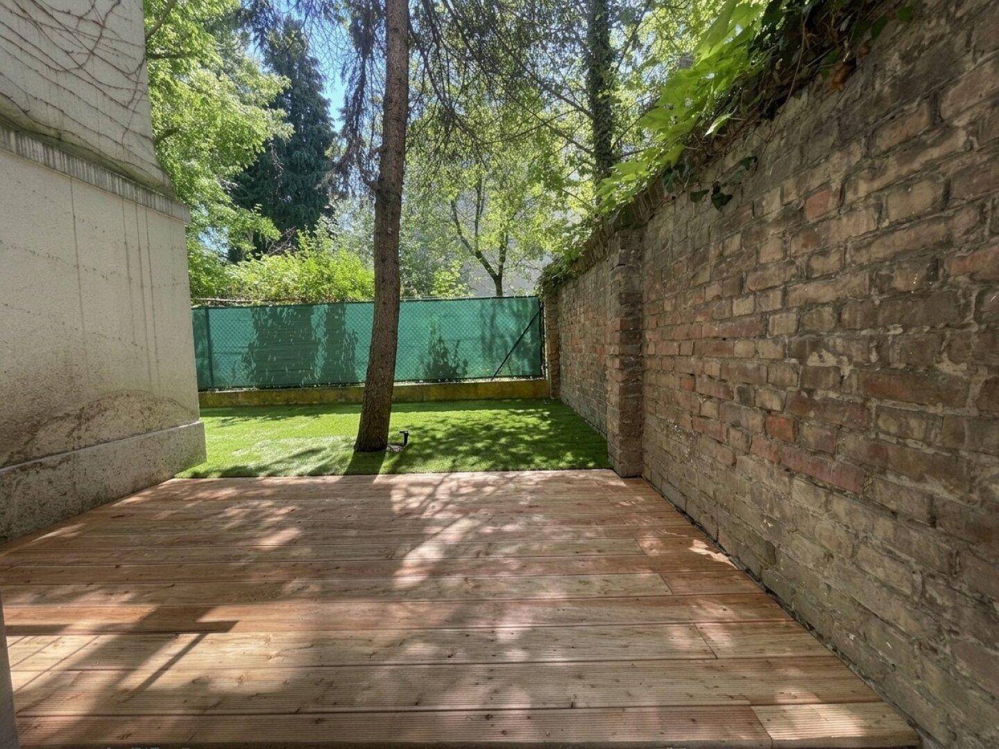 Holzterrasse im Freien mit angrenzendem Rasen und einer Ziegelmauer, ideal zum Entspannen.
