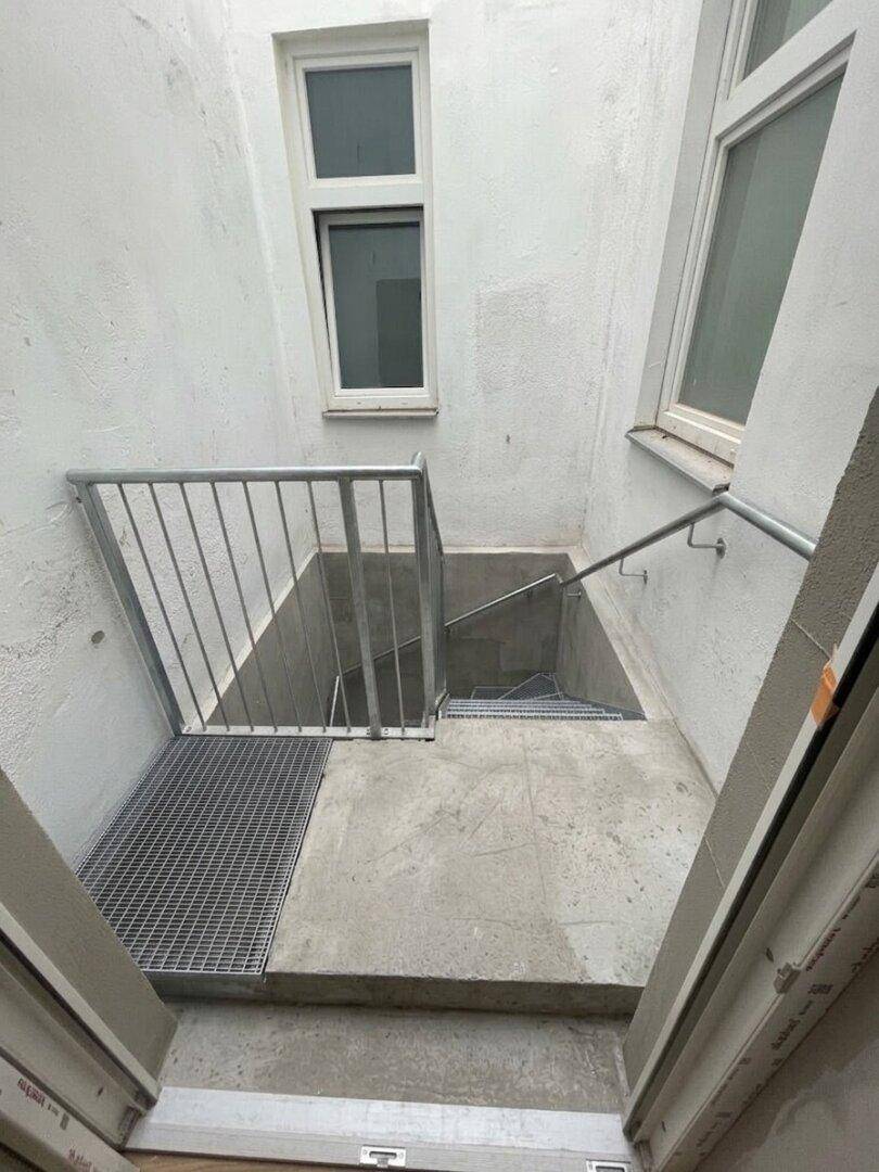 Außentreppe aus Beton mit Metallgeländer, führt zu einem unteren Bereich des Gebäudes.