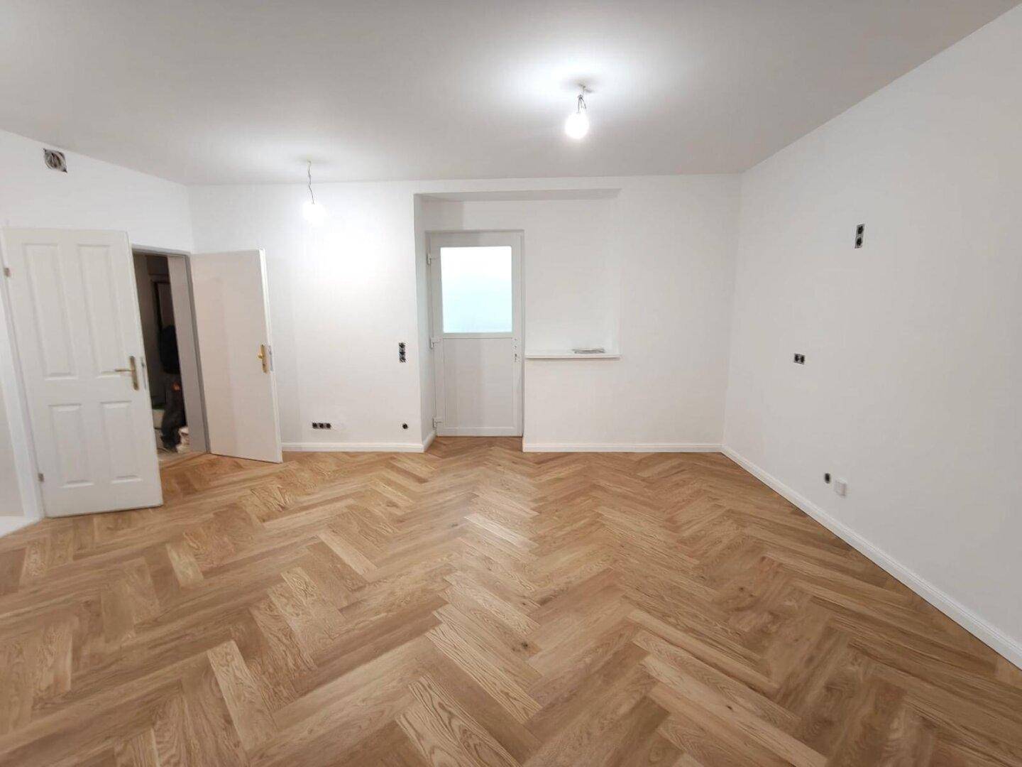 Großes, helles Zimmer mit Fischgrätparkett und weiß gestrichenen Wänden, bietet viel Raum.