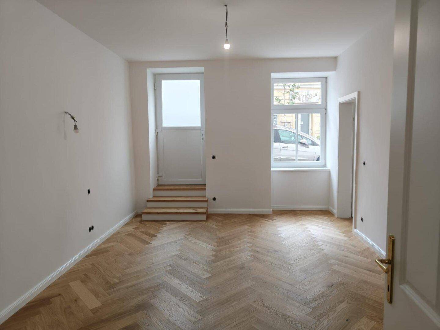 Helles Zimmer mit Fischgrätparkett und Zugang zu einem Außenbereich, ideal für Wohnzwecke.