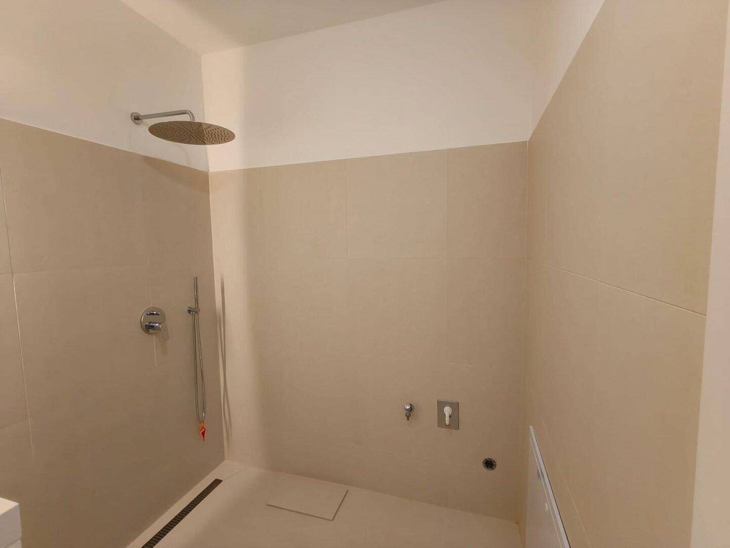Modernes Badezimmer mit Regendusche und neutralen Fliesen, bietet eine minimalistische Ästhetik.