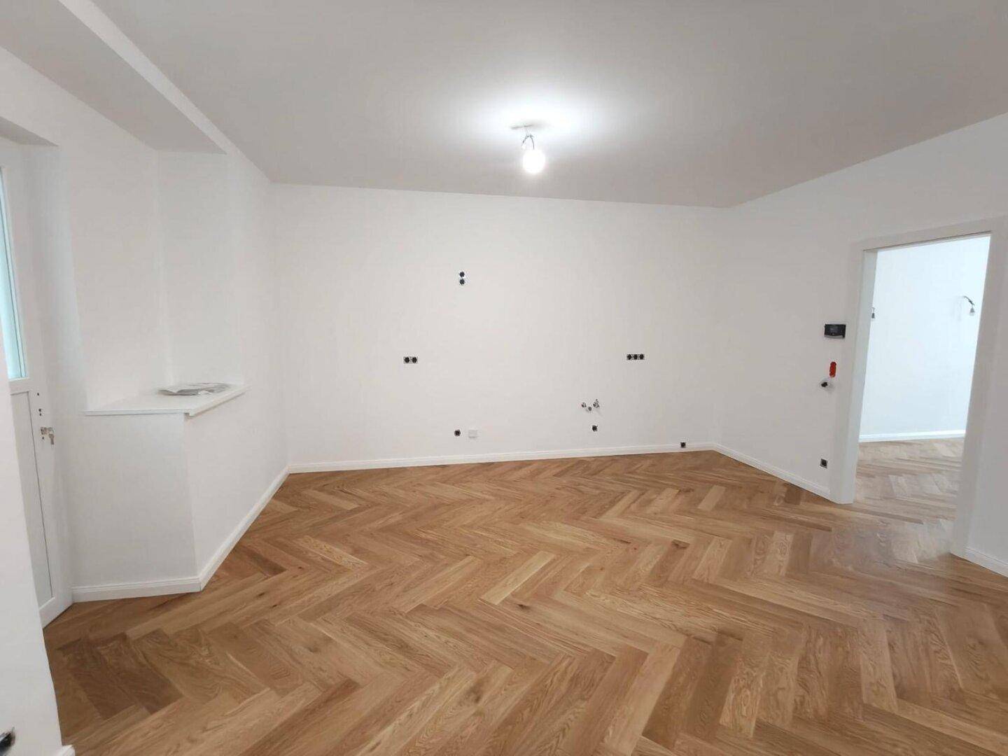 Helles Zimmer mit Fischgrätparkett und weiß gestrichenen Wänden, bereit zur individuellen Gestaltung.