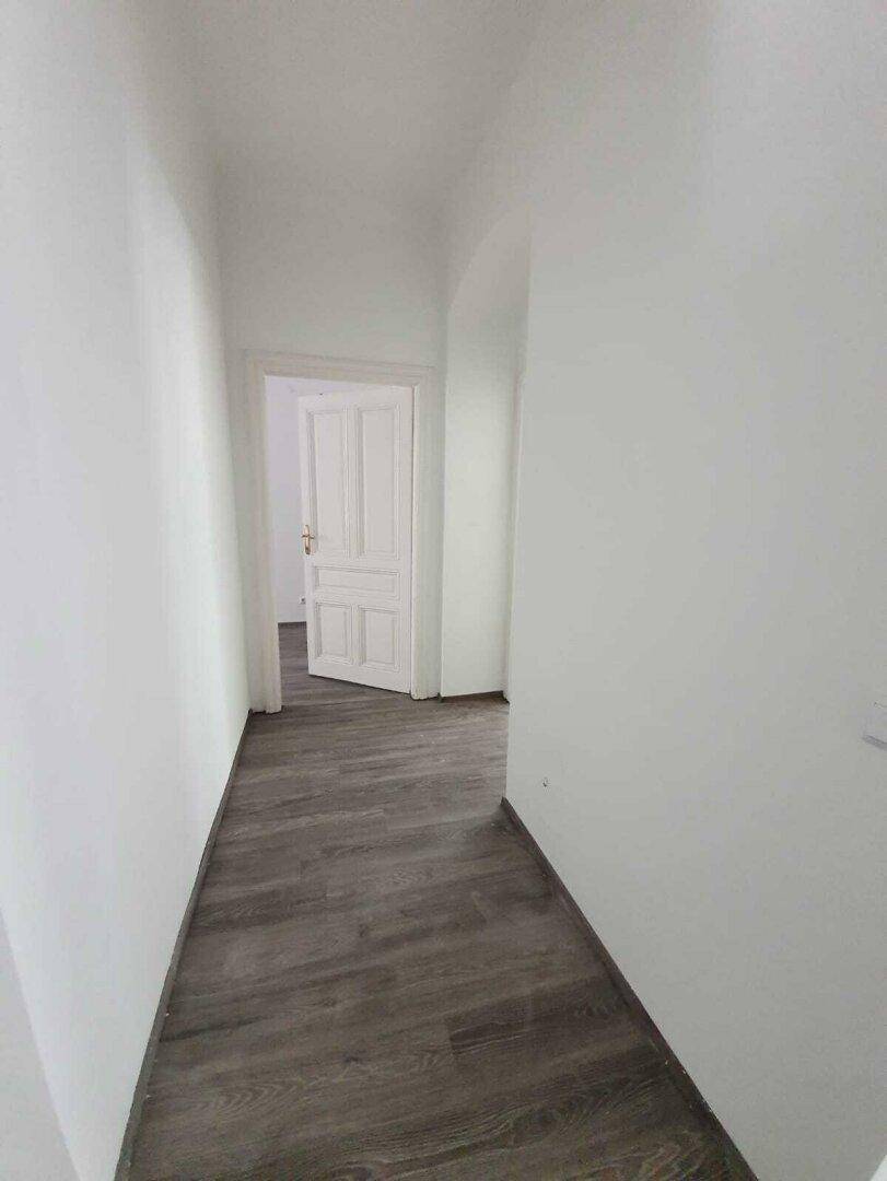 Schmaler Flur mit dunklem Laminatboden und weißen Wänden, der zu weiteren Räumen führt.