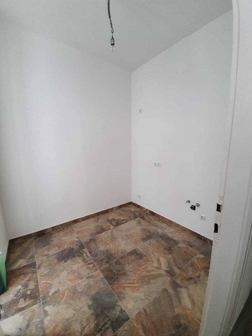 Kleiner Raum mit gemusterten Fliesen und Anschlüssen für eine zukünftige Küche.