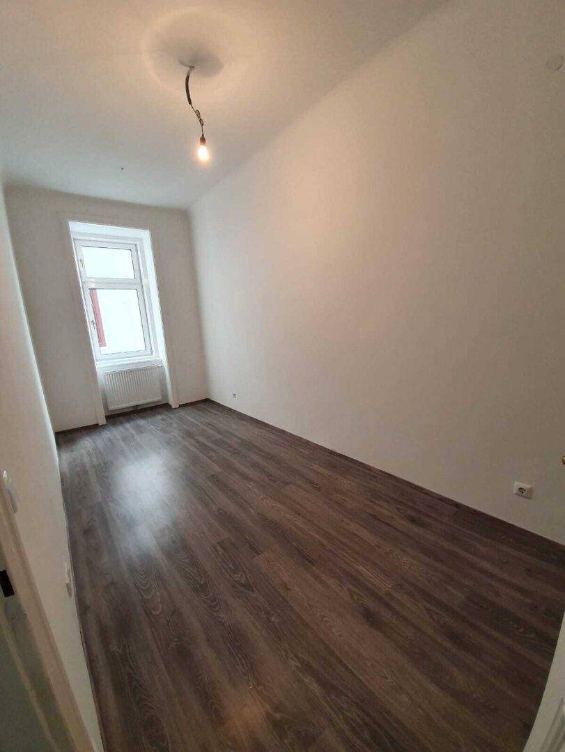 Leeres Schlafzimmer mit dunklem Laminatboden, weiß gestrichenen Wänden und einem Fenster.
