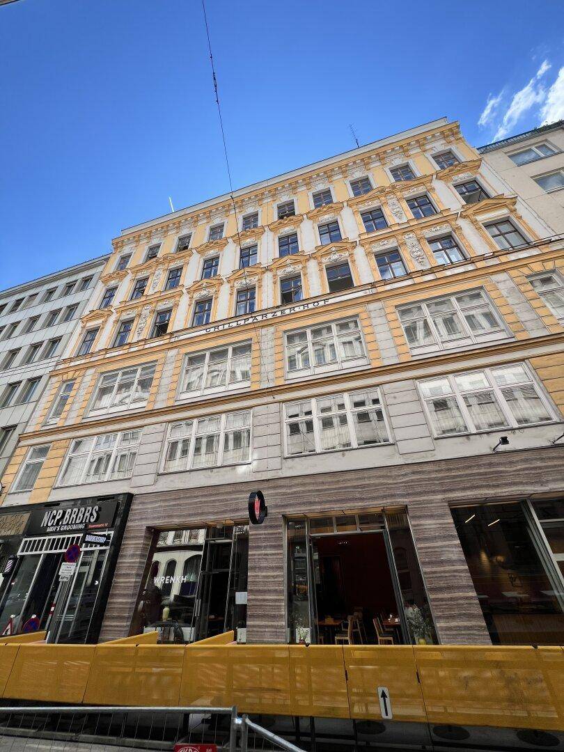 Städtisches Gebäude mit klassischer Architektur, gelber Fassade und Geschäften im Erdgeschoss unter klarem Himmel.