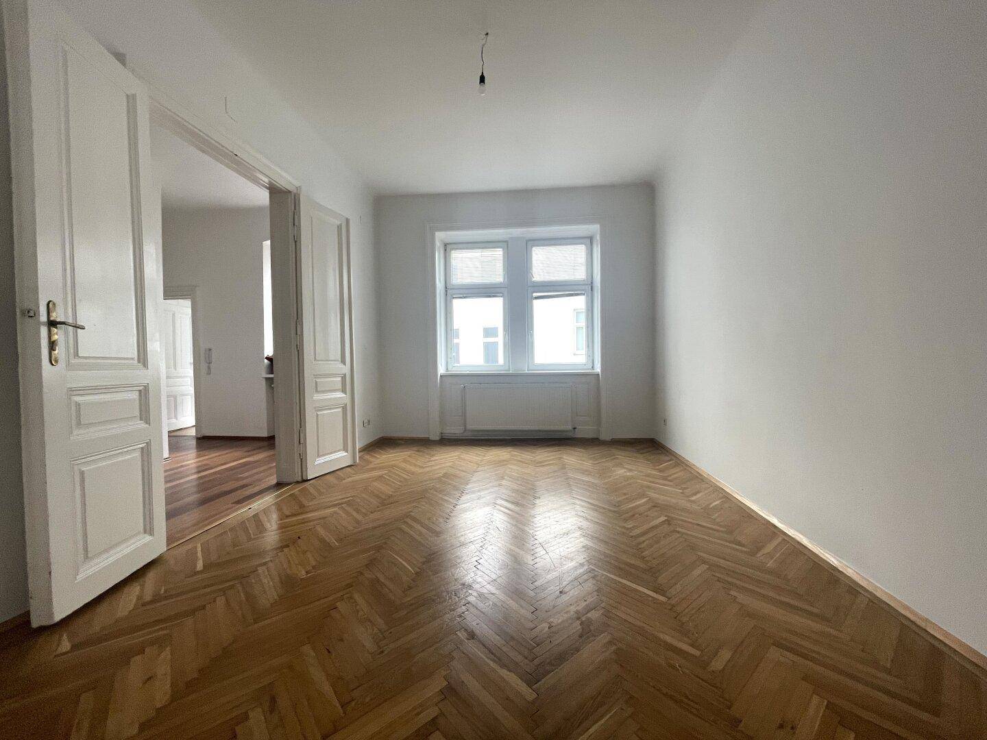 Helles Zimmer mit Fischgrätparkett und weißen Wänden, bereit zur individuellen Gestaltung und Nutzung.