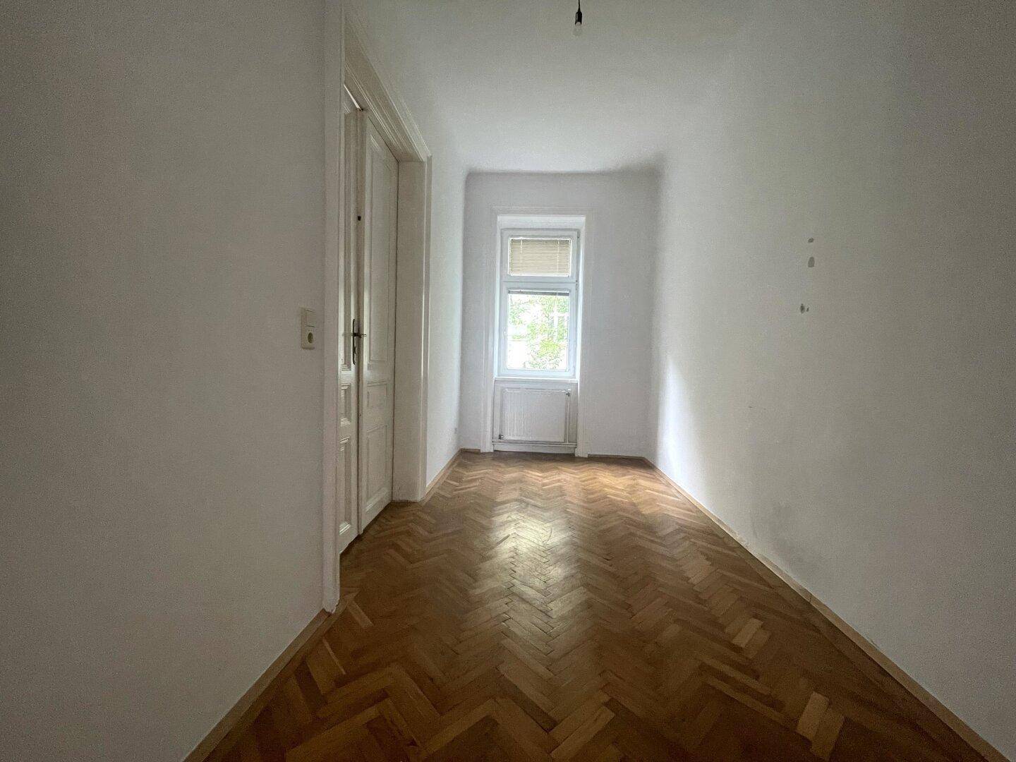 Kleineres Zimmer mit Fischgrätparkett und einem Fenster, ideal als Schlaf- oder Arbeitszimmer nutzbar.