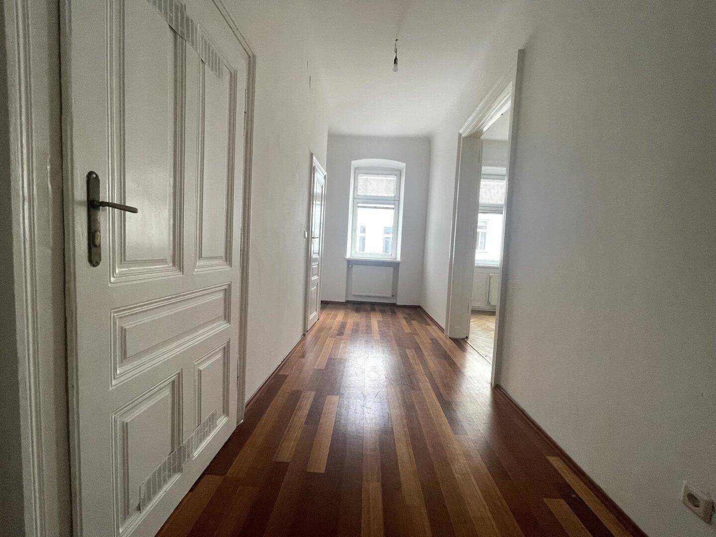 Langer Flur mit Holzdielenboden und hohen weißen Türen, der zu weiteren Räumen führt.