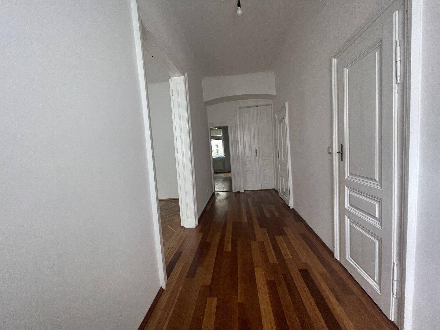 Heller Flur mit Holzdielenboden und klassischen Türen, der verschiedene Bereiche der Wohnung verbindet.