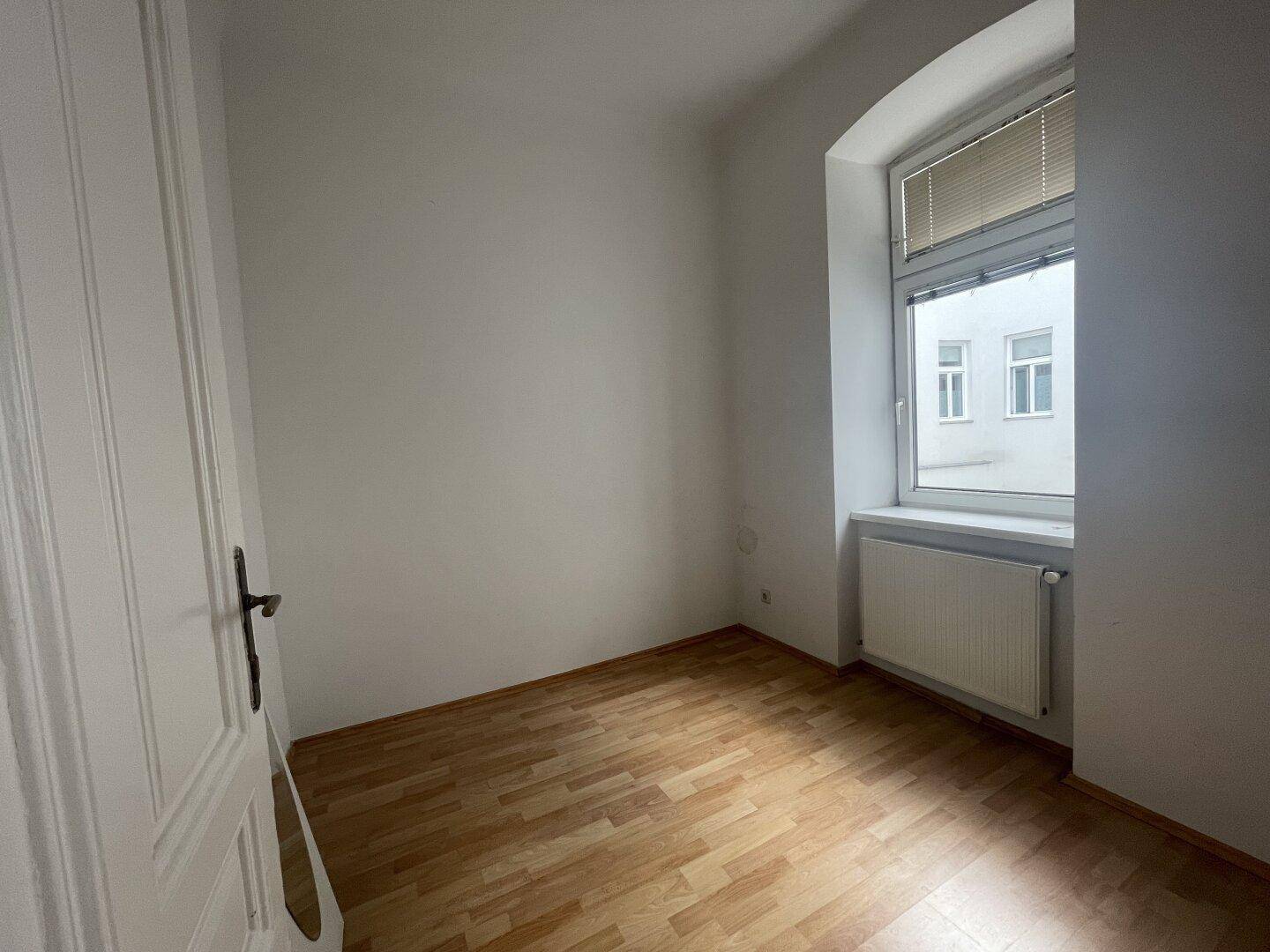 Helles Zimmer mit Holzboden und einem Fenster, das sich gut als Kinder- oder Gästezimmer eignet.