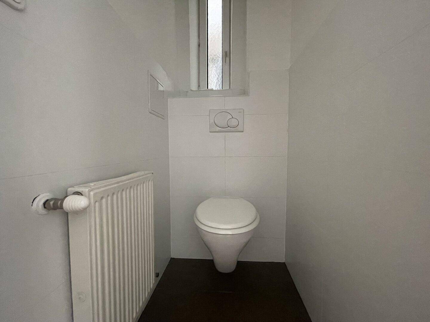 Separates WC mit wandhängender Toilette und kleinem Fenster für Belüftung und Tageslicht.
