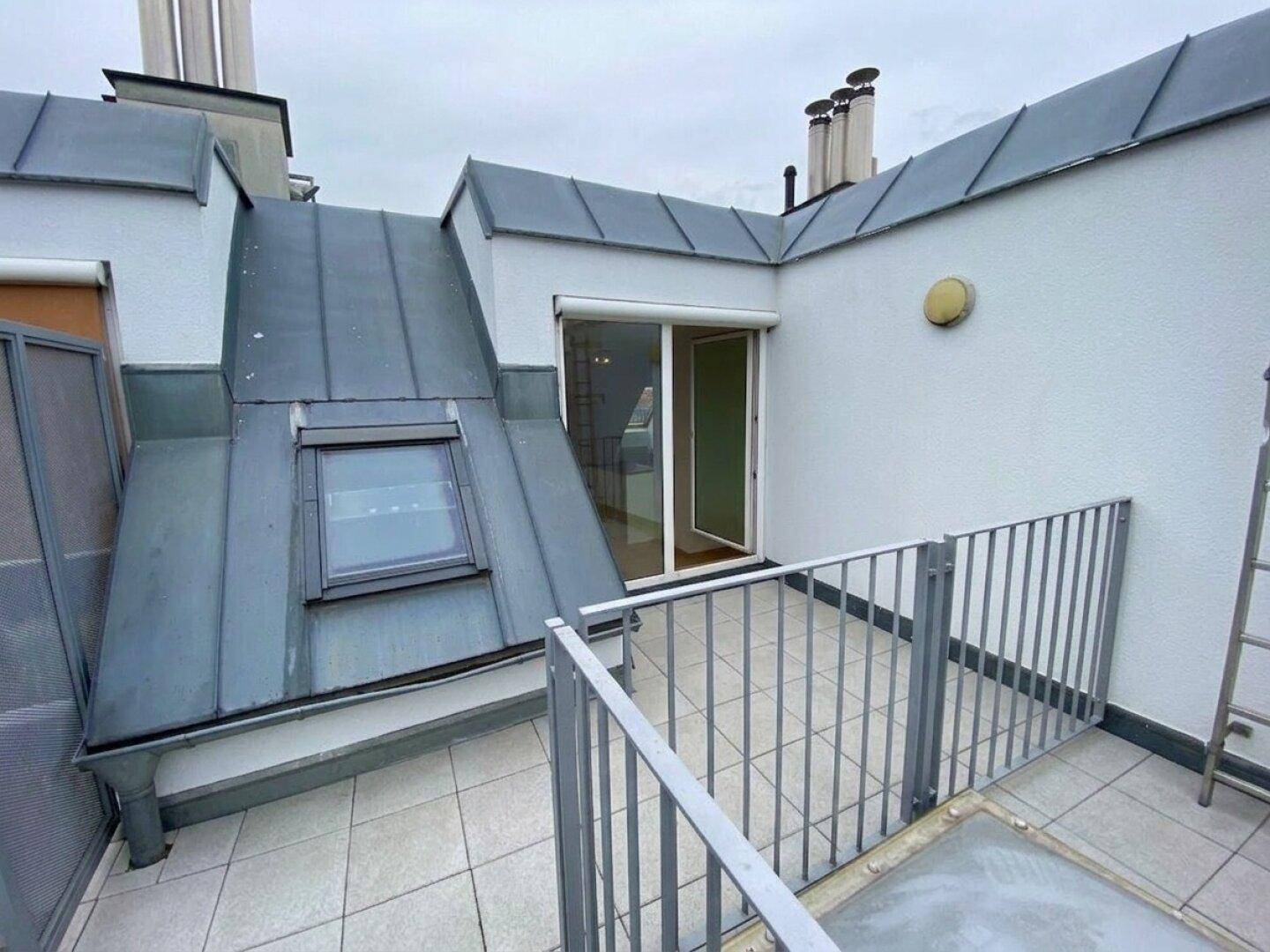 Kleine Dachterrasse mit Metallgeländer und Zugang zu einem Dachgeschossraum, mit Dachfenster.