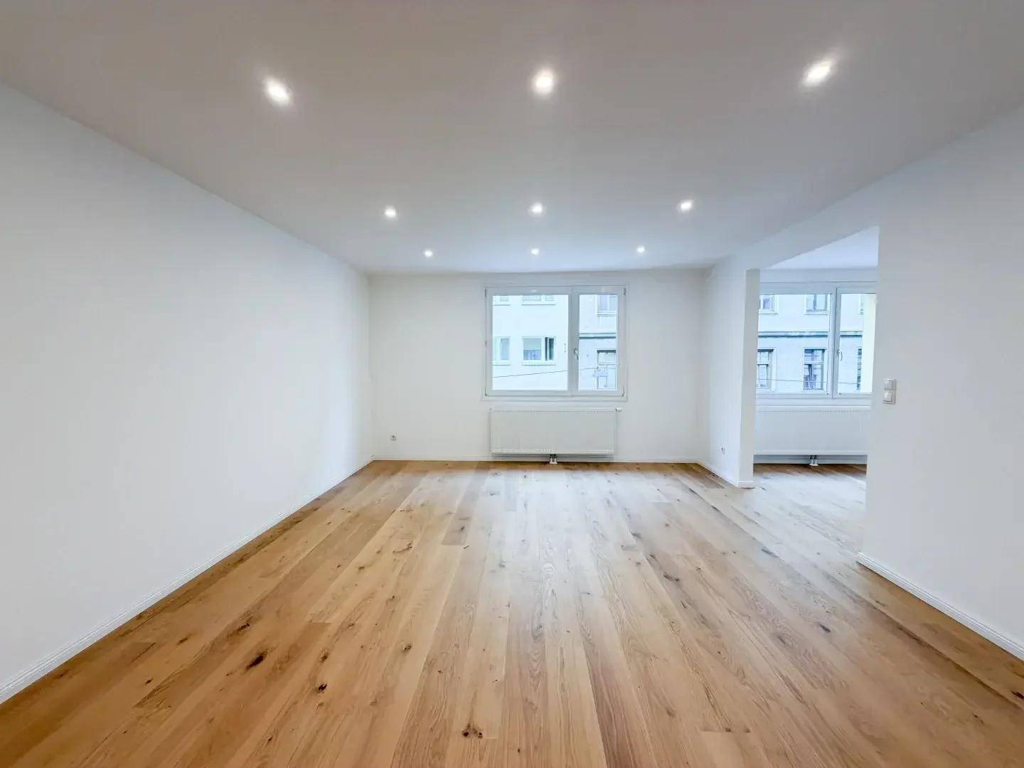 Heller, leerer Raum mit modernem Holzparkettboden und Einbaustrahlern an der Decke.