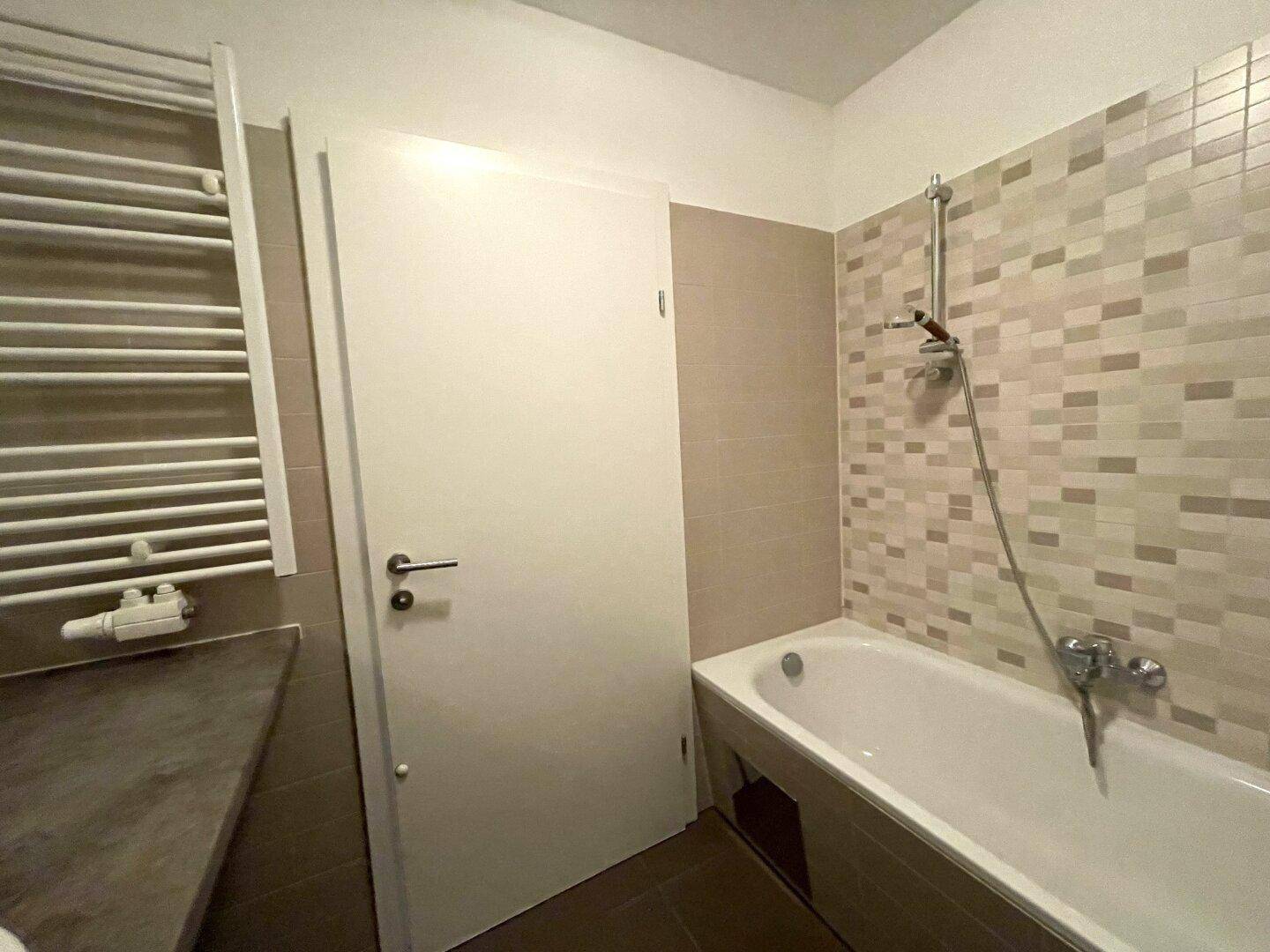 Badezimmer mit Badewanne, beigefarbenen Fliesen und praktischem Handtuchheizkörper.