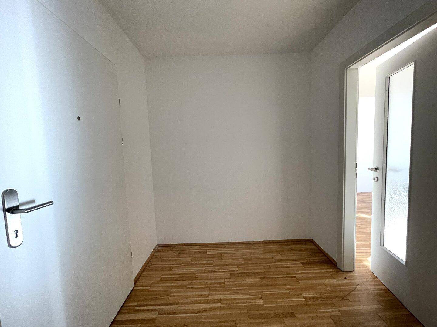 Heller Flur mit Parkettboden und weißen Wänden, der zu weiteren Räumen führt.