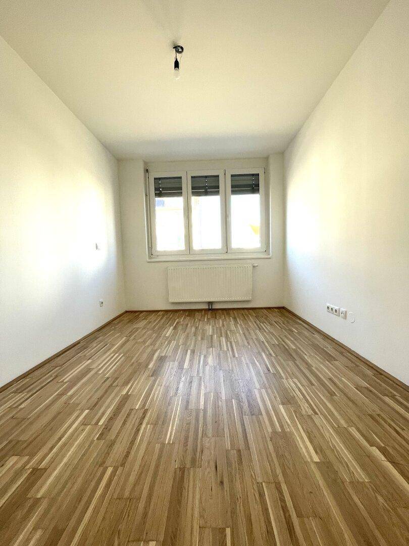 Ruhiges Schlafzimmer mit Parkettboden, weißen Wänden und Fenster mit Jalousien.