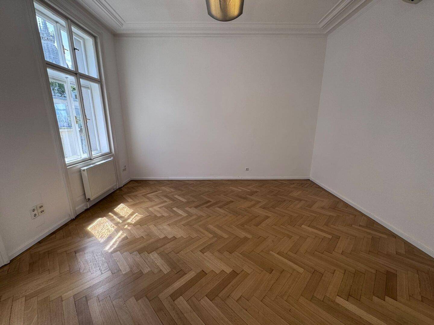 Leerer Raum mit elegantem Fischgrätparkett und hohen Decken, bereit für individuelle Gestaltung.
