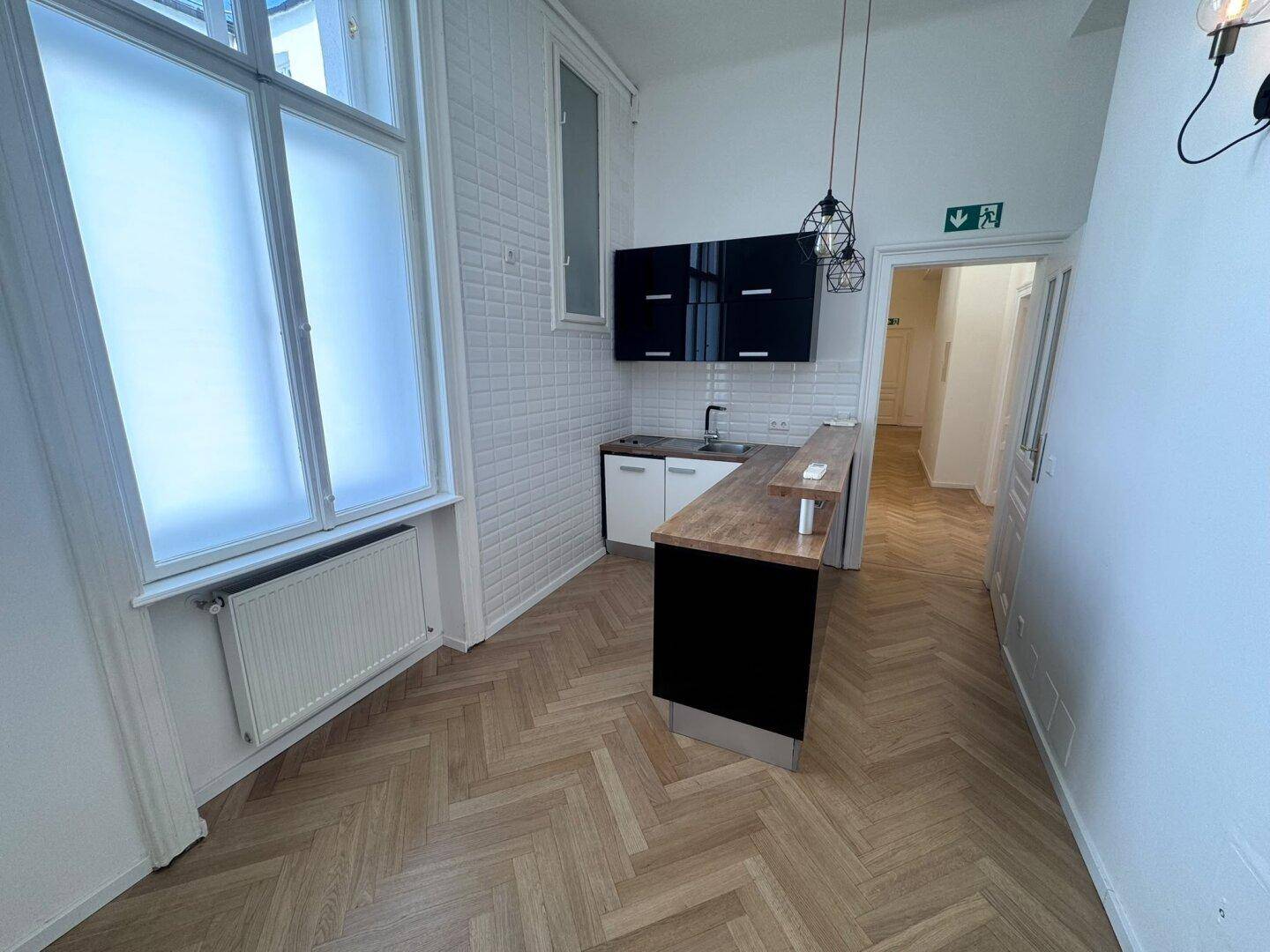 Kleine Küchenzeile mit schwarzem Hochglanz und Holztheke in einem hellen Raum mit Fischgrätparkett.