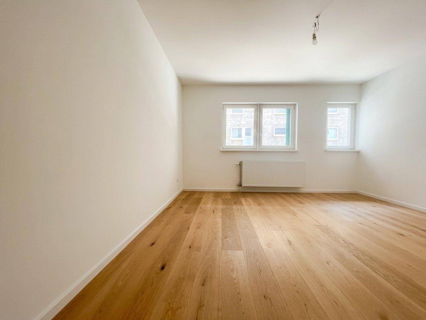 Heller, leerer Raum mit neuem Holzfußboden und zwei Fenstern.
