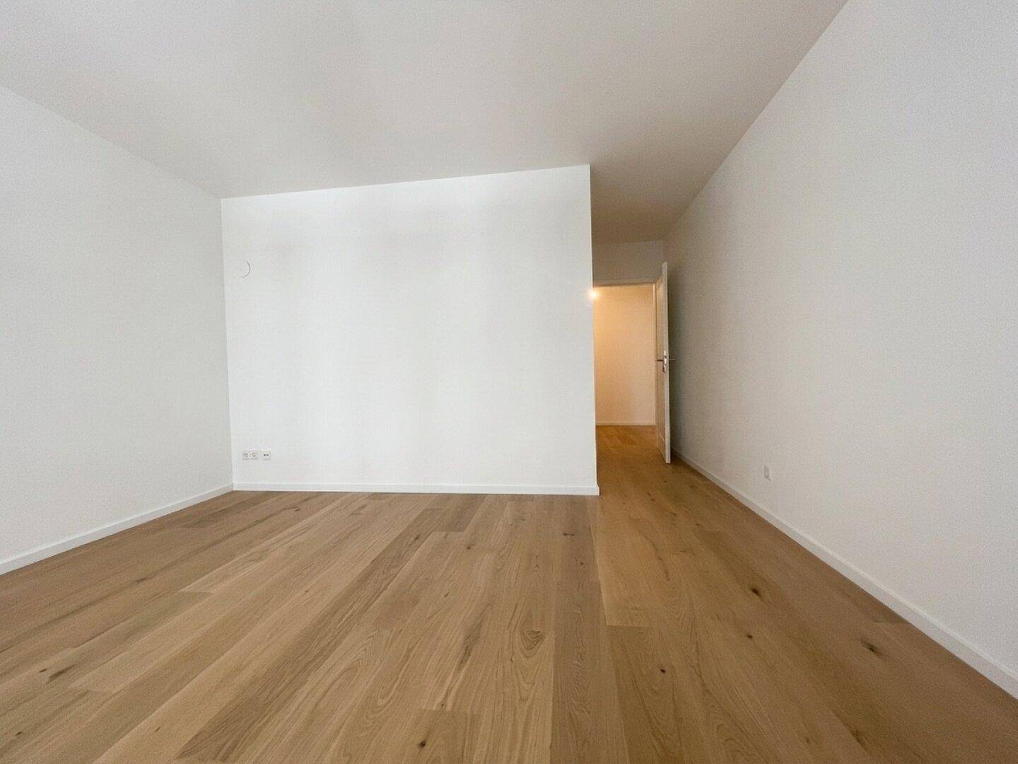 Geräumiger, heller Raum mit Holzparkett und Zugang zu einem weiteren Bereich.