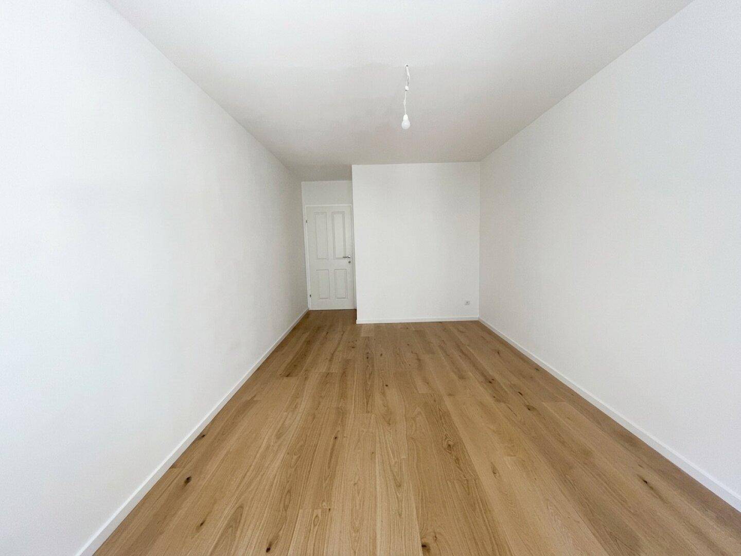 Langer, heller Raum mit Holzfußboden und einer weißen Tür am Ende.