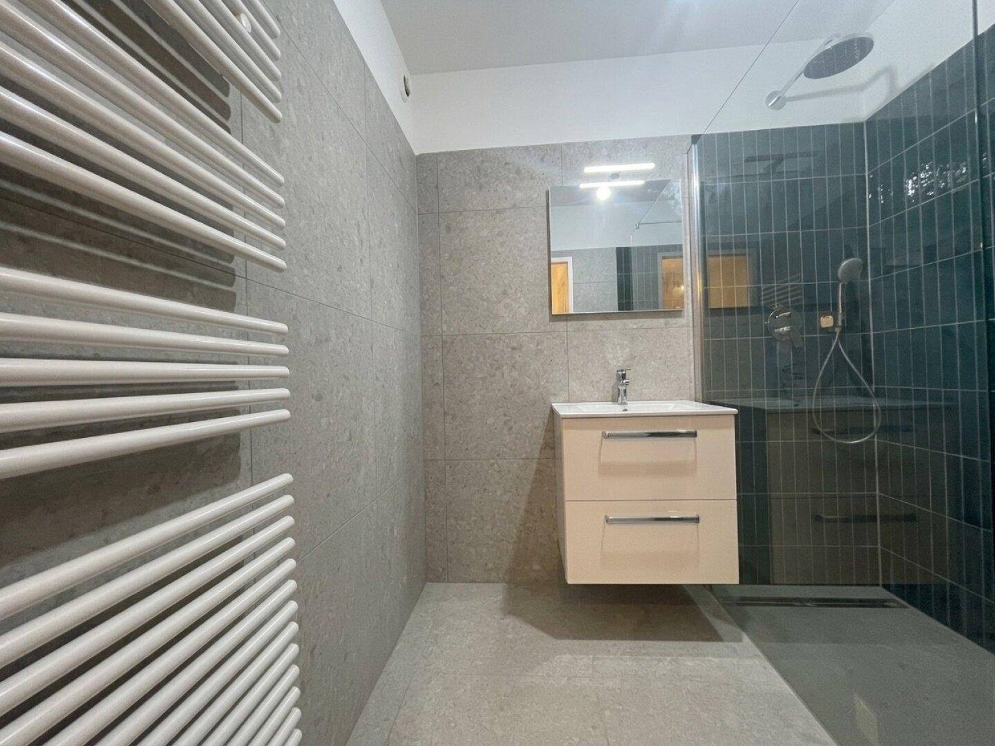 Modernes Badezimmer mit grauen Fliesen, begehbarer Dusche und beheiztem Handtuchhalter.