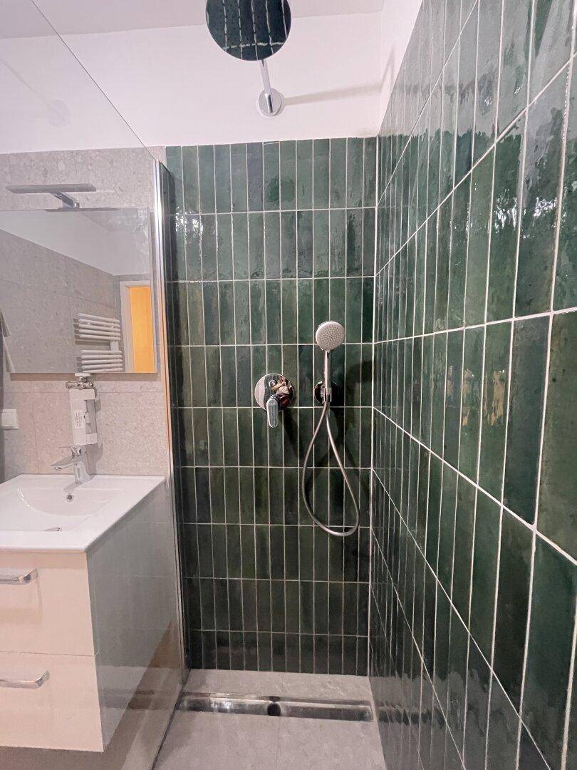 Moderne begehbare Dusche mit dunkelgrünen Fliesen und Regenduschkopf.