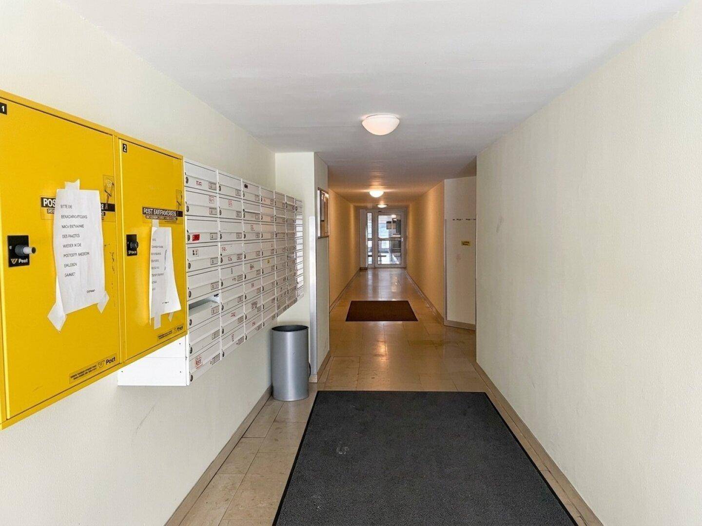 Langer Flur im Eingangsbereich mit vielen Briefkästen und gelben Postfächern.