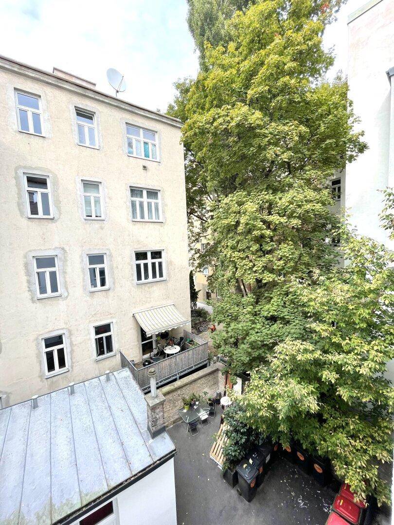 Innenhofansicht mit üppigem Grün und einem kleinen Balkon an einem der Wohngebäude.