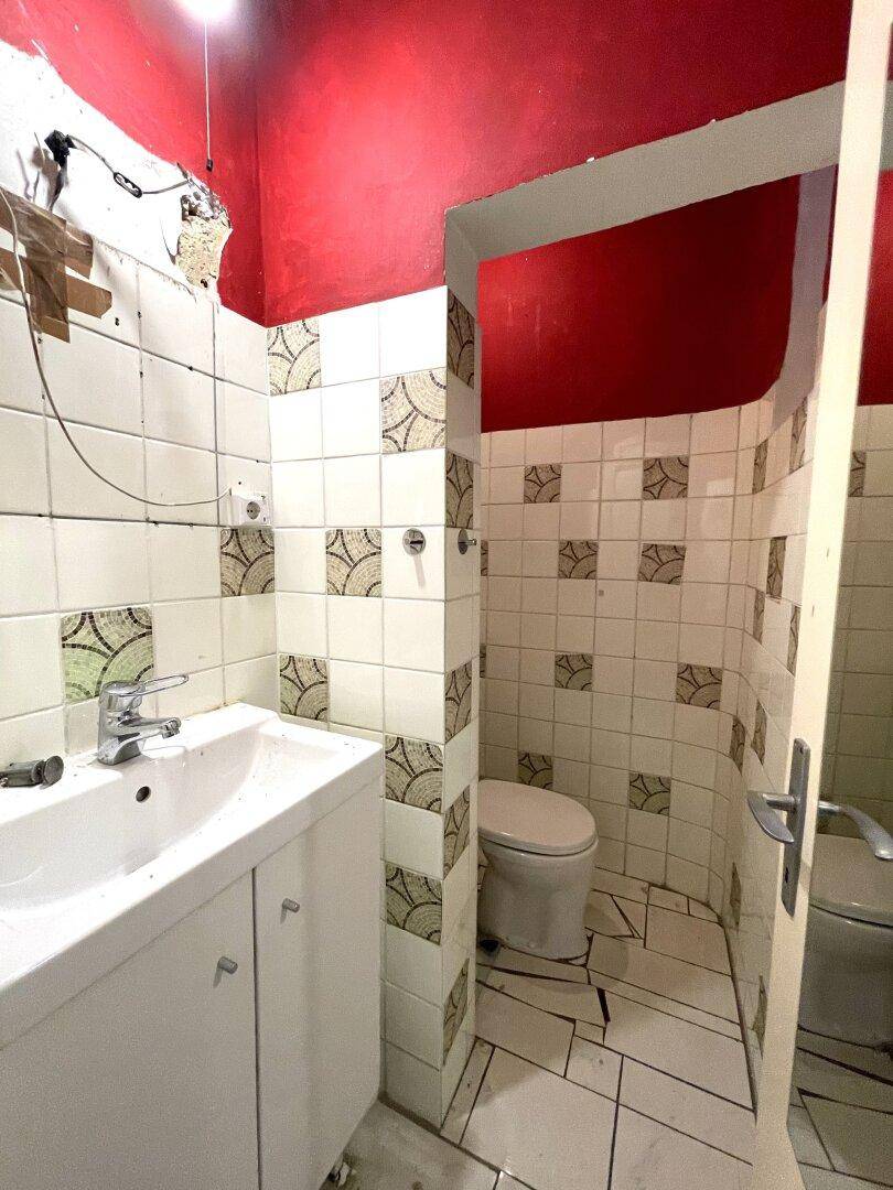 Badezimmer mit Waschbecken, Toilette und alten Fliesen in Rot und Weiß, renovierungsbedürftig.