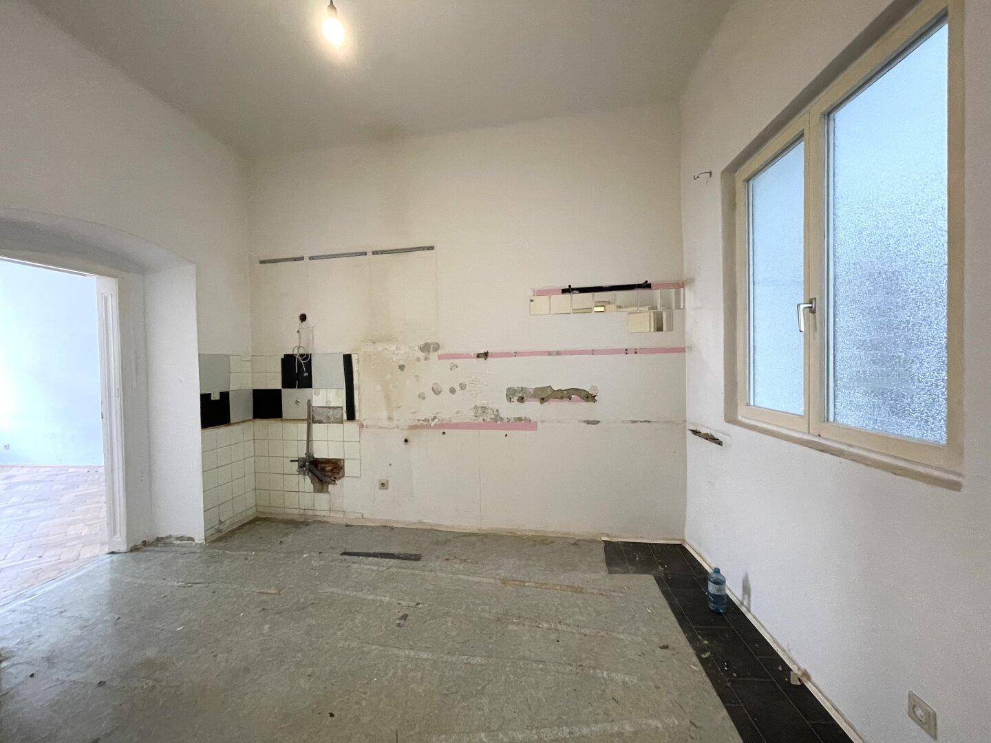 Renovierungsbedürftige Küche mit alten Fliesen, einem Fenster und Spuren früherer Installationen.