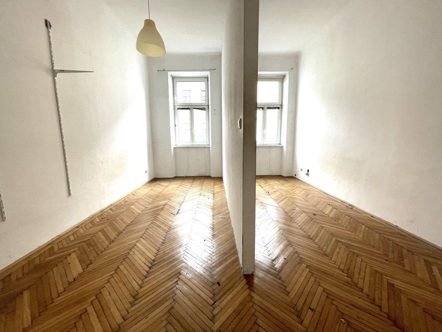Helles Zimmer mit Fischgrätparkett und einer Trennwand, die den Raum unterteilt.