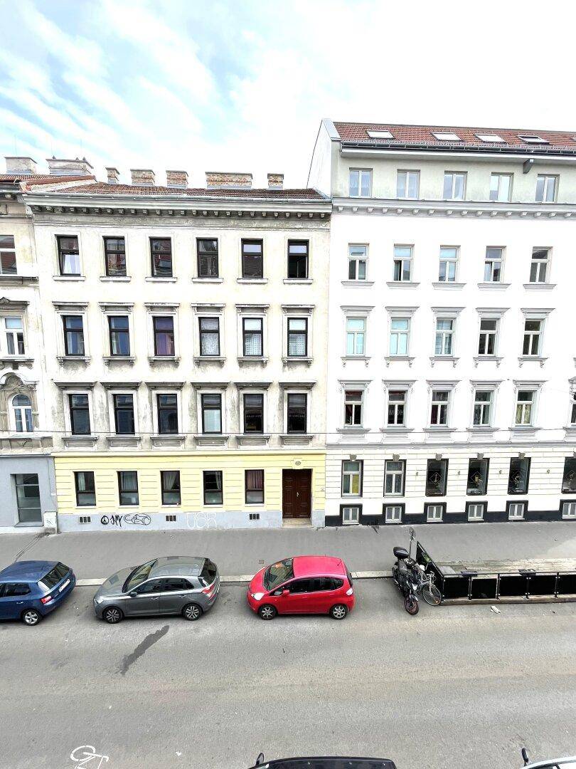 Straßenansicht mit geparkten Autos und traditionellen Wohngebäuden unter bewölktem Himmel.