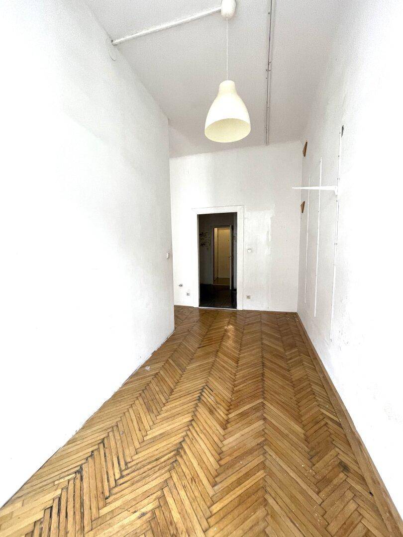 Langer Raum mit Fischgrätparkett und einem Durchgang zu einem weiteren Bereich der Wohnung.