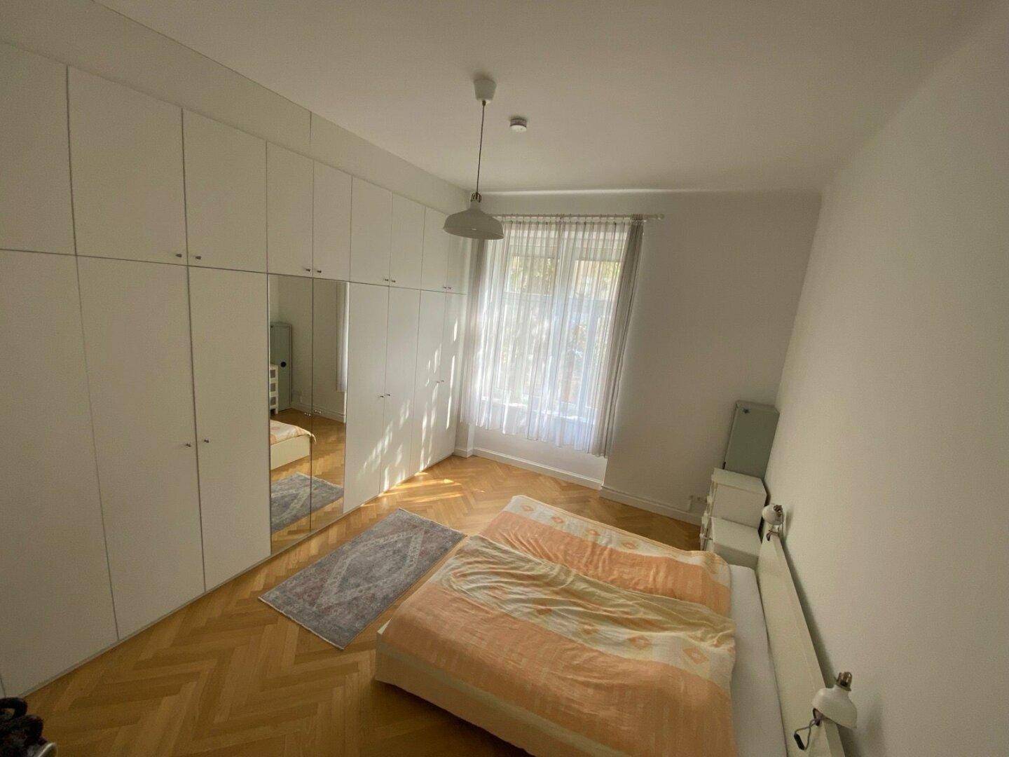 Helles Schlafzimmer mit modernen Einbauschränken, Spiegeln und Fischgrätparkettboden.