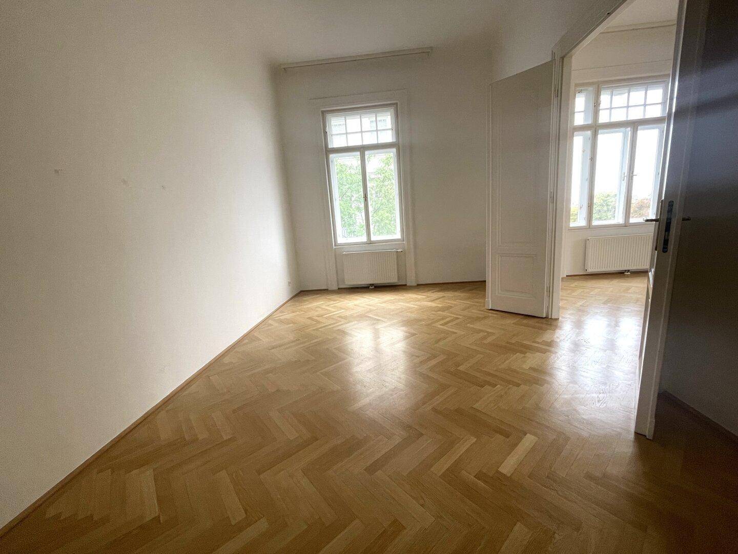 Leeres Zimmer mit Fischgrätparkett, weißen Wänden und einem Fenster, ideal als Schlaf- oder Arbeitszimmer.