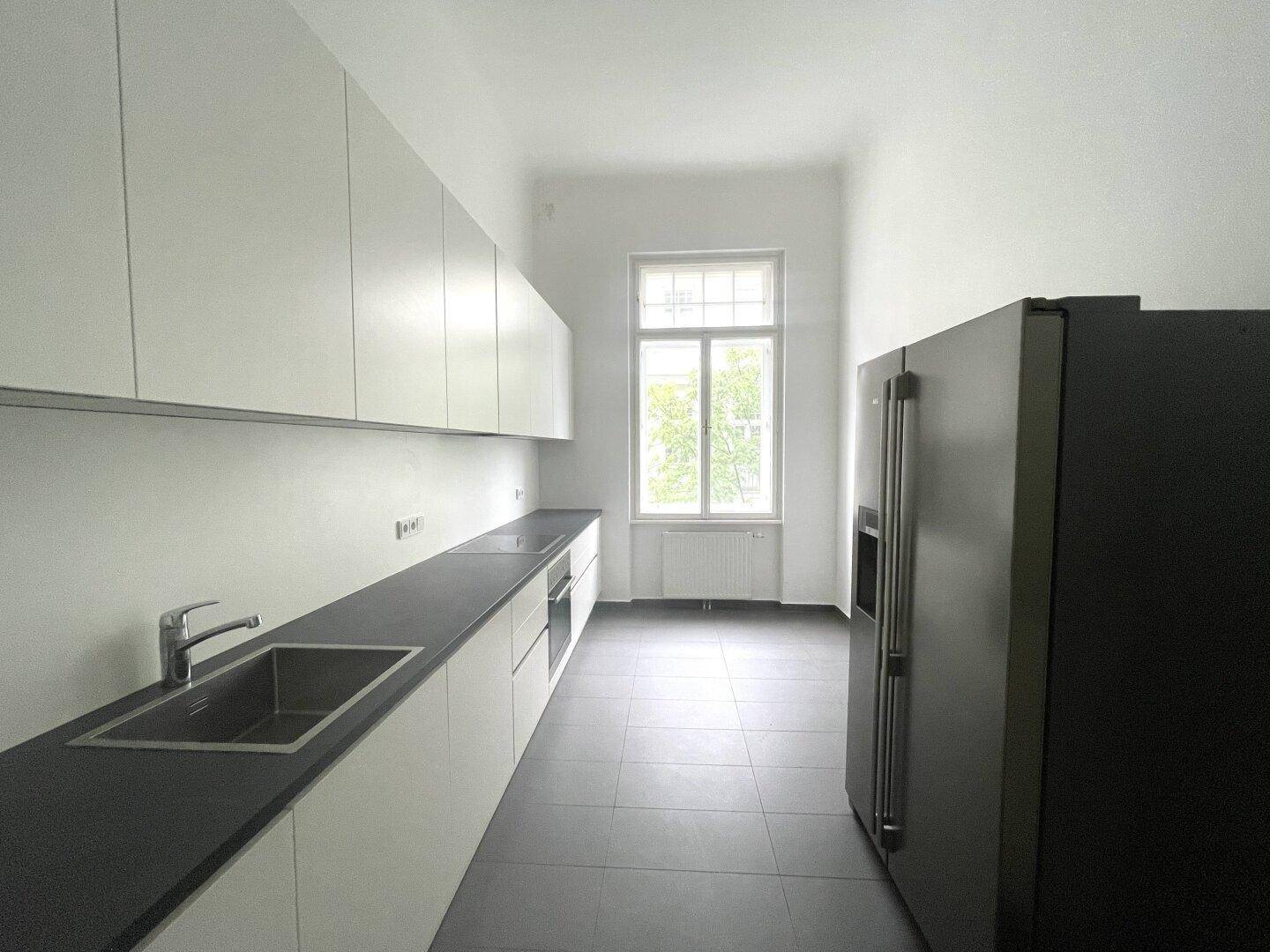 Moderne Küche mit weißen Schränken, dunkler Arbeitsplatte, Spüle und großem schwarzem Kühlschrank.