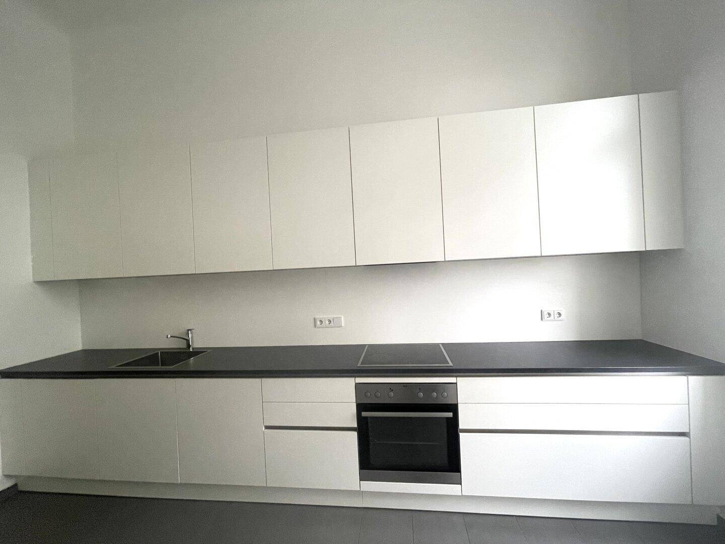 Detailansicht der modernen Küche mit weißen Schränken, dunkler Arbeitsplatte, Induktionskochfeld und Backofen.