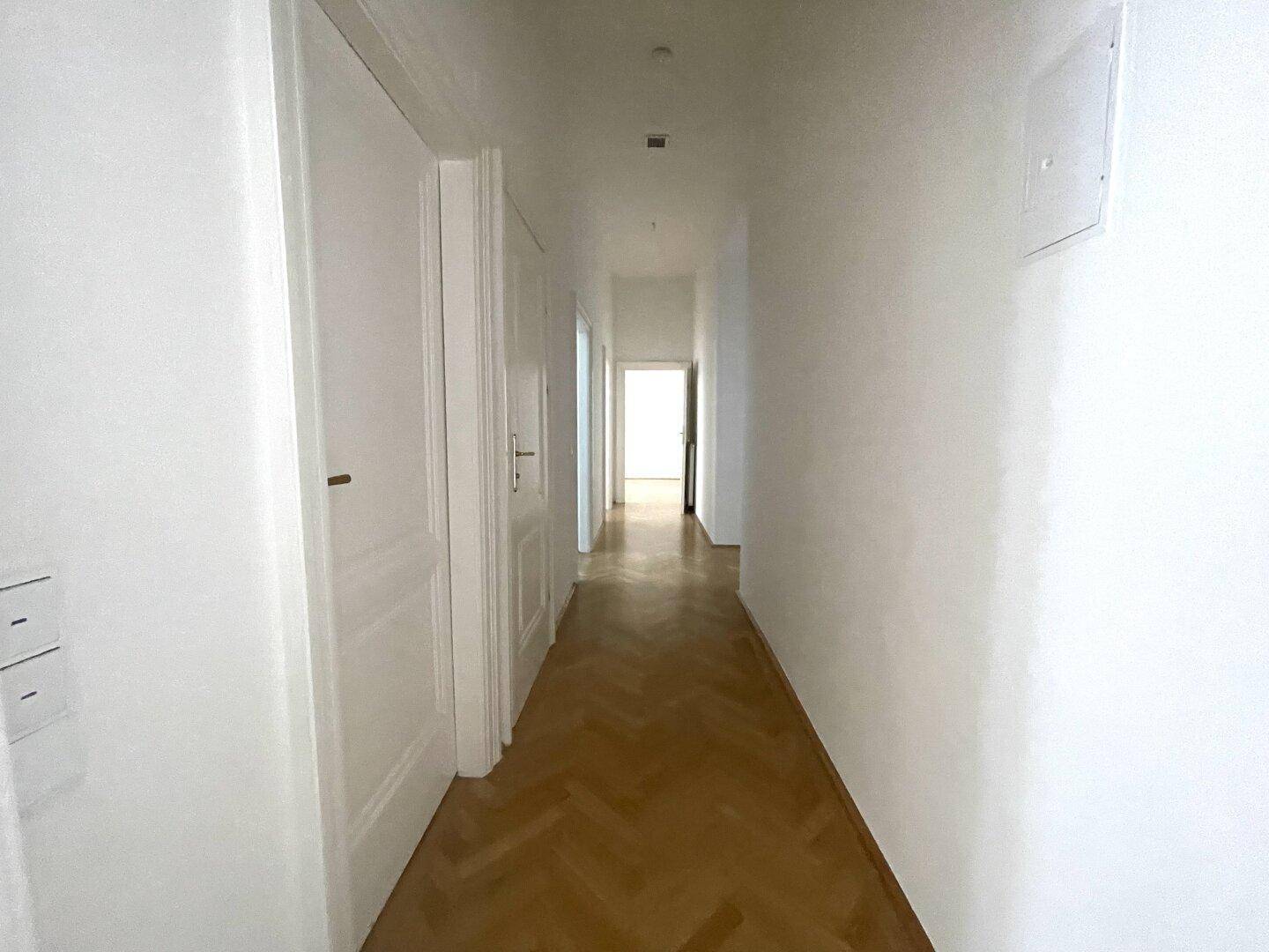 Langer, heller Flur mit Fischgrätparkett und mehreren Türen, die zu den angrenzenden Räumen führen.