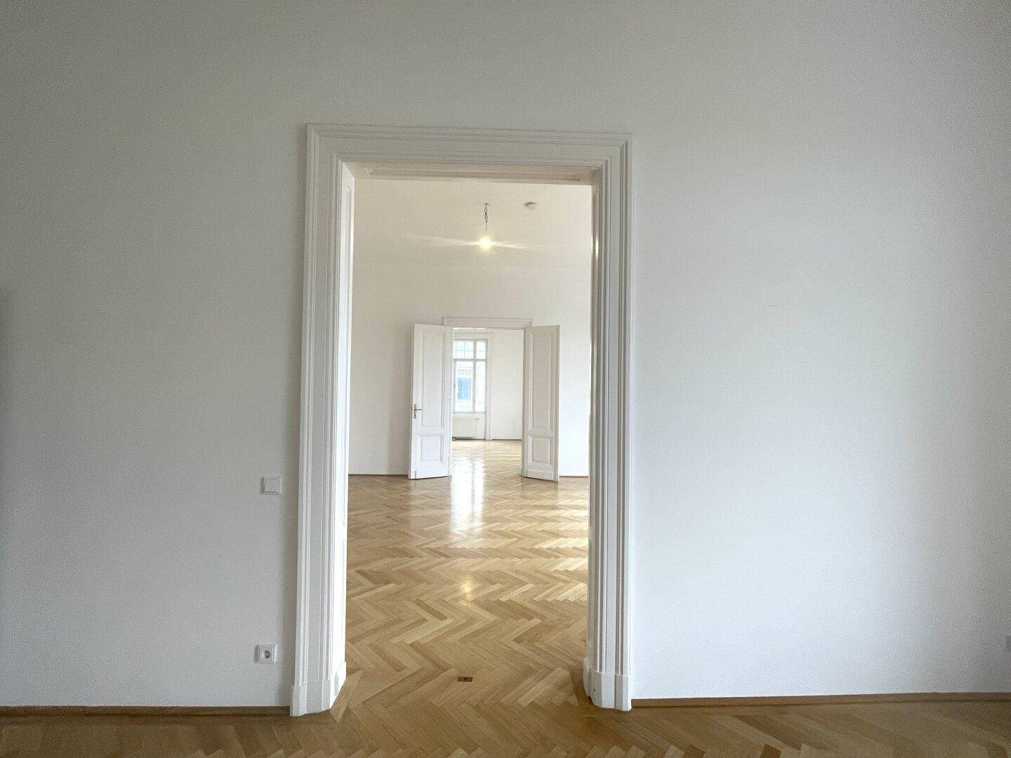 Blick durch eine elegante Türöffnung in einen weiteren Raum mit glänzendem Fischgrätparkett.