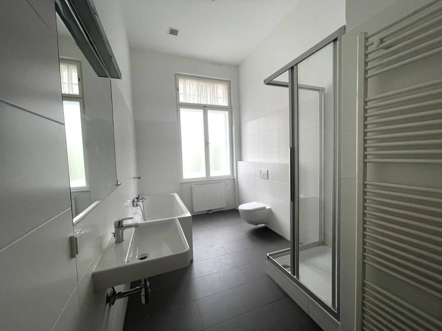 Modernes Badezimmer mit dunklen Fliesen, Badewanne, Dusche, WC, Einzelwaschbecken und Fenster.
