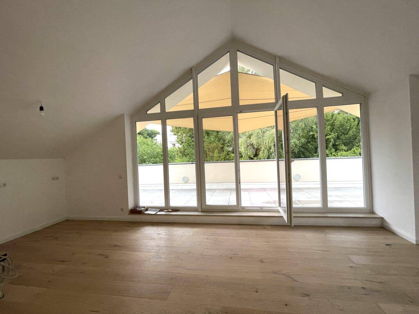 Heller Wohnraum mit Eichenparkett, großen Fenstern und Zugang zur Terrasse mit Grünblick.