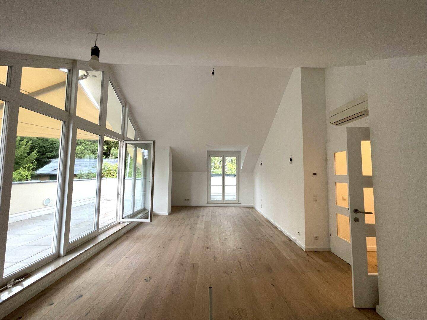 Geräumiger Wohnbereich mit hellem Parkettboden, Dachschrägen und Klimaanlage.