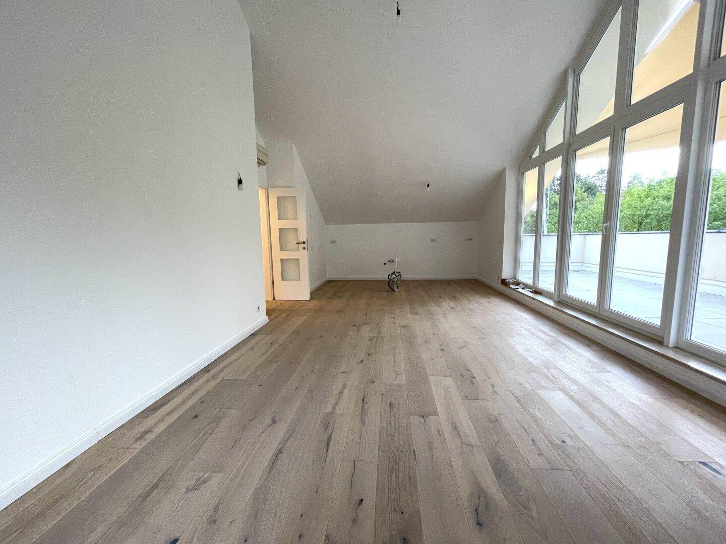 Heller, leerer Raum mit breiter Fensterfront, Eichenparkett und Dachschrägen.