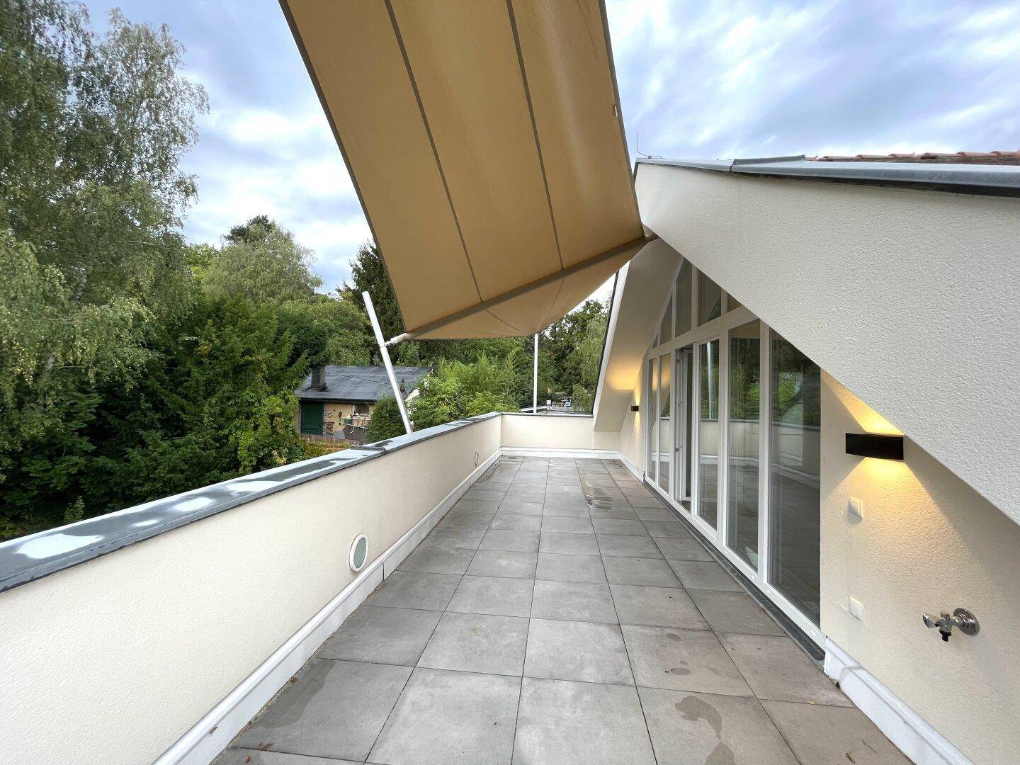 Große geflieste Terrasse mit ausfahrbarer Markise und Blick auf grüne Umgebung.