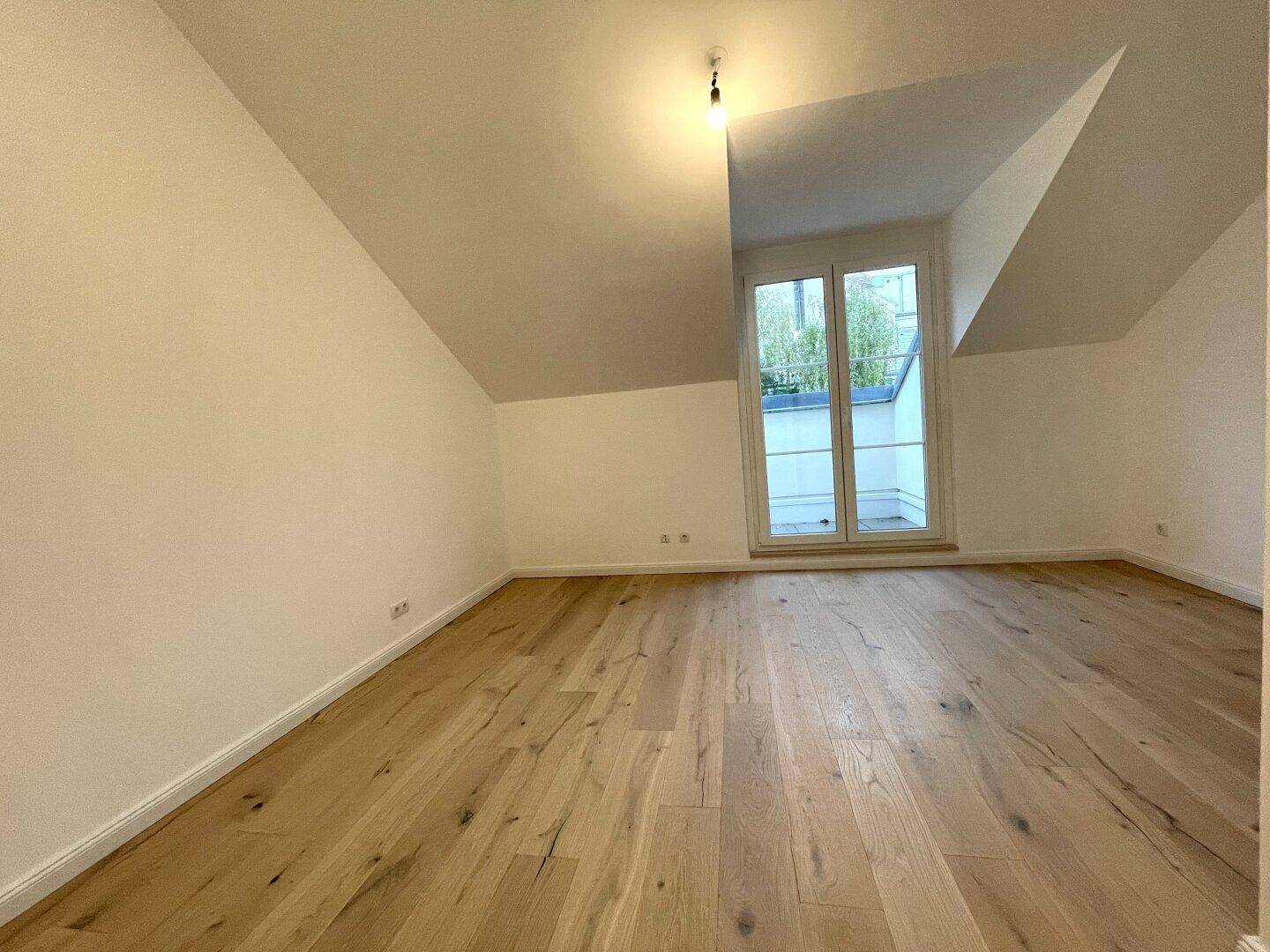 Helles Schlafzimmer mit Eichenparkett, Dachschrägen und Zugang zu einem kleinen Außenbereich.
