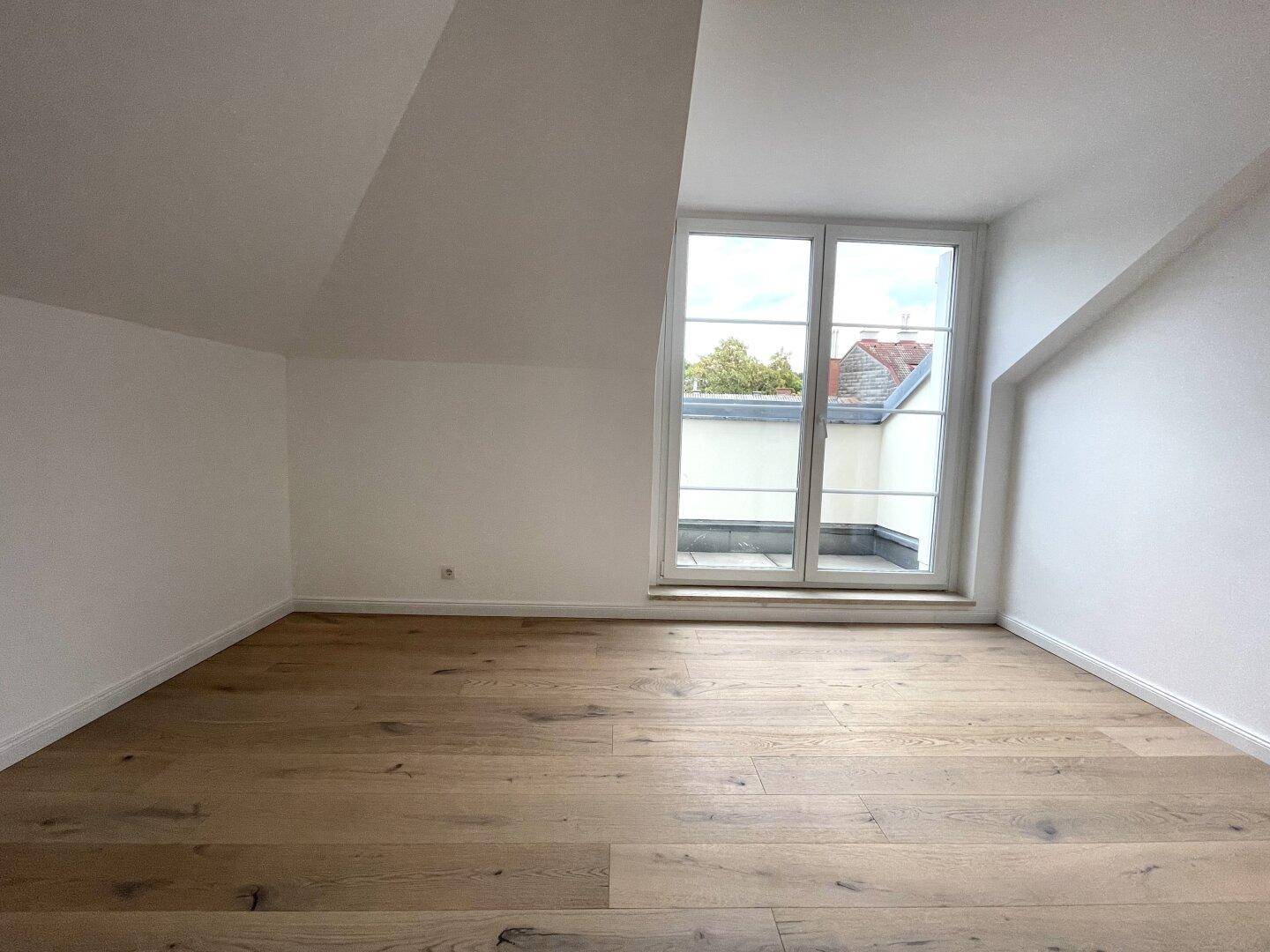 Helles Schlafzimmer mit Eichenparkett, Dachschrägen und Zugang zu einem kleinen Außenbereich.