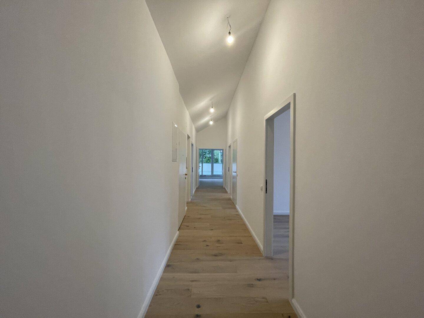 Langer, heller Flur mit Eichenparkettboden und Dachschrägen, der zu mehreren Räumen führt.